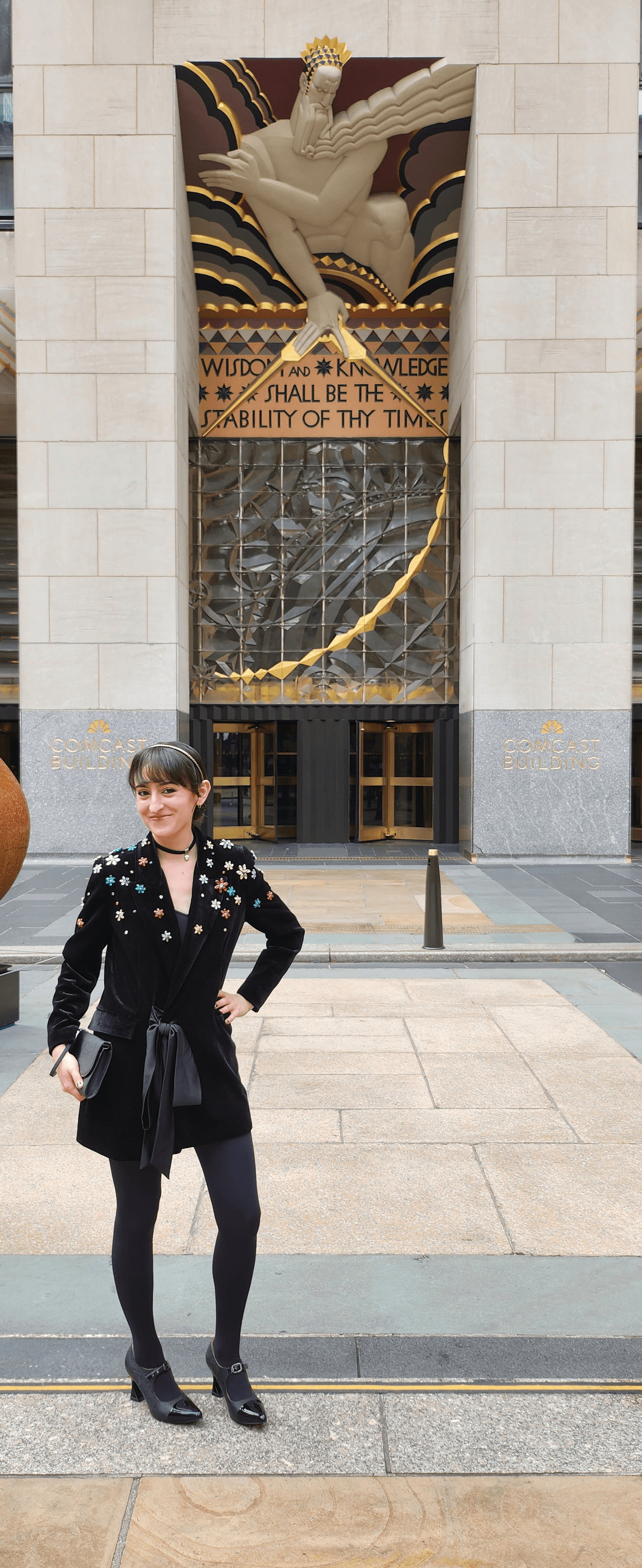 Woman in a black floral blazer posing before the Art Deco Comcast Building entrance.